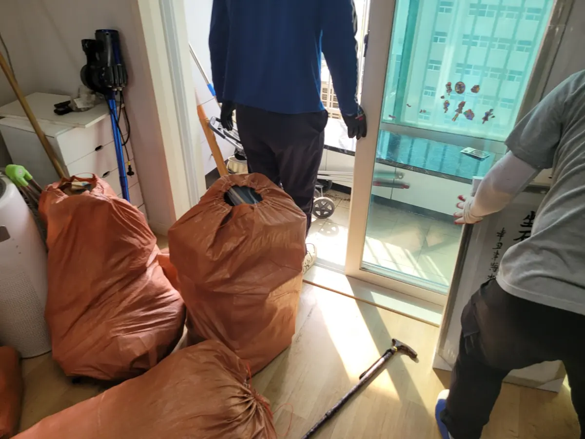 작업자가 자루에 담은 생활물품을 들고 베란다 문 쪽으로 이동하는 반출 작업