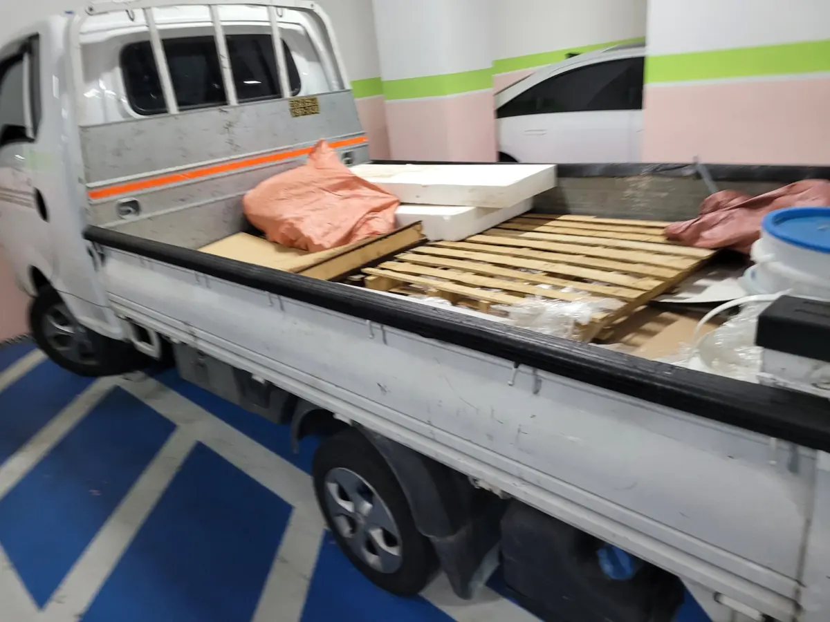 아파트 지하주차장에 세운 작업 차량 적재함에 자루와 판재, 팔레트를 실은 집정리 서비스 현장