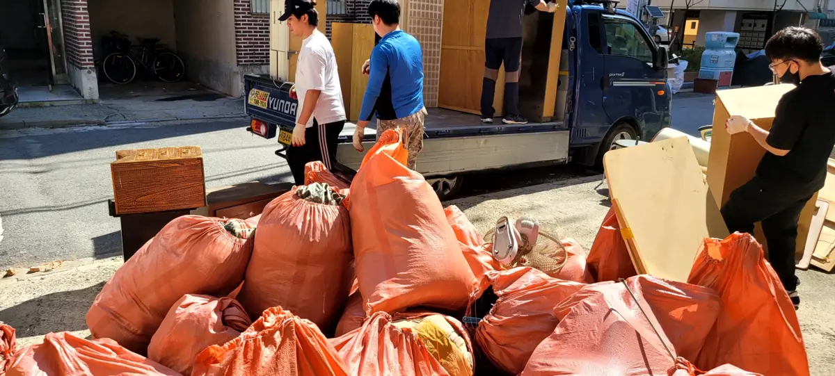 이사 후 골목에 가구와 생활물품이 쌓이고 작업자들이 차량에 싣는 집정리 현장