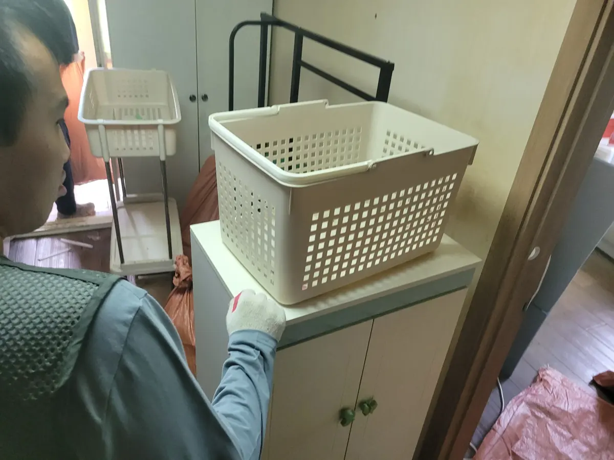 작업자가 주방 수납장 위의 바구니를 들어 생활물품을 분류하는 집정리 현장