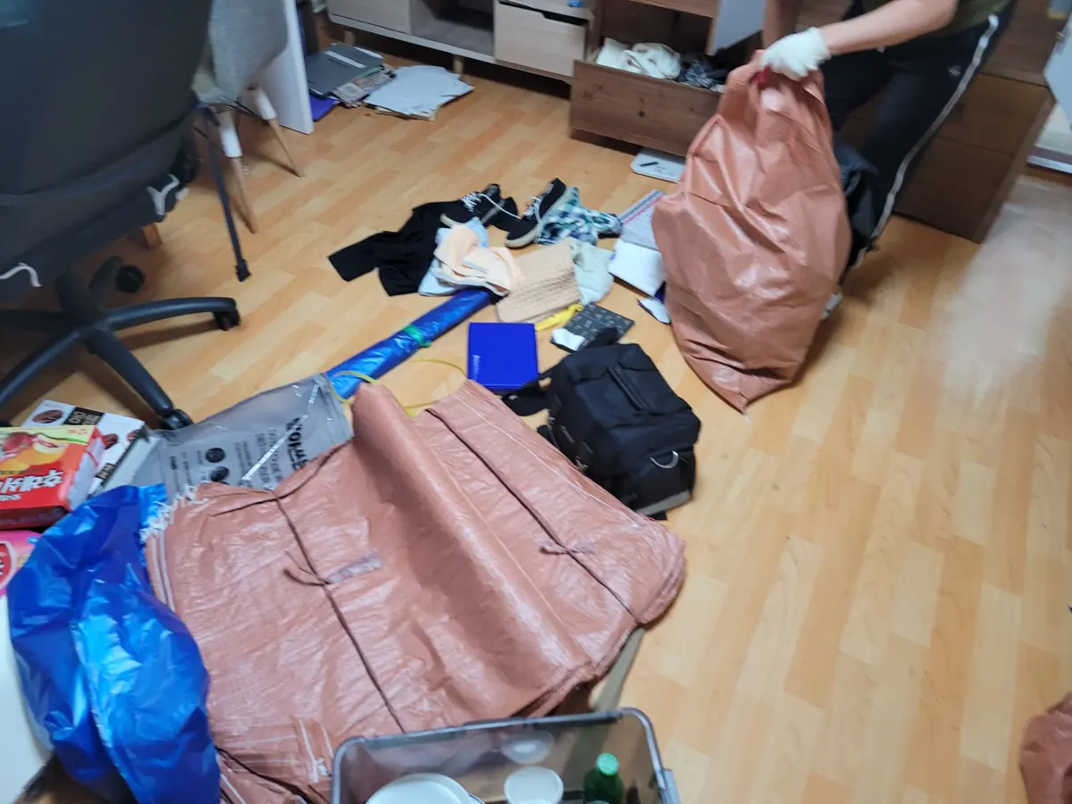 원룸 바닥에 옷과 물품이 흩어져 있고 작업자가 자루에 담고 있는 집정리 작업 현장